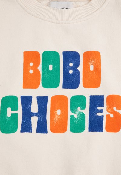 Suéter crema con texto grande y en negrita que dice “BOBO CHOSES” en naranja, verde, azul y un azul más oscuro. Textura de tela suave, diseño de cuello redondo.