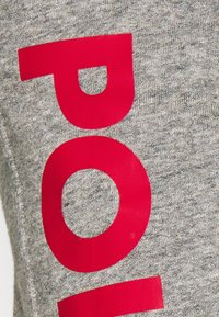 Grått tyg med stora, djärva röda bokstäver. Texturen verkar mjuk och stickad, utan synliga mönster eller dekorationer.