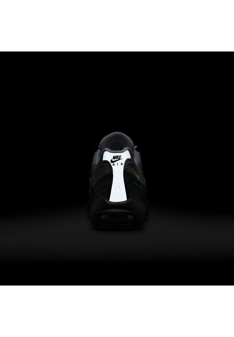 Zapatillas Nike negras con un upper texturizado, un panel en el talón reflexivo en blanco y acentos verdes; diseño minimalista con bordes suaves.