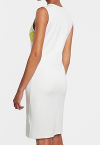 Robe blanche sans manches avec une silhouette ajustée, présentant un motif floral jaune à l'avant et une texture de tissu lisse.