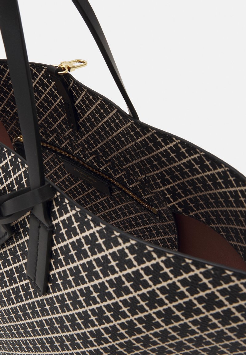 Black and beige tote bag featuring a geometric pattern, leather straps, and a zippered interior pocket with a contrasting brown lining.