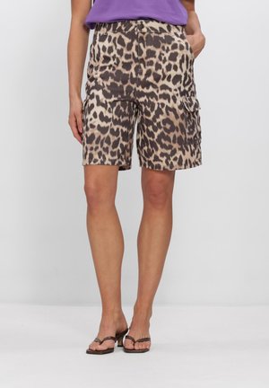 Vrouw die knielange cargoshorts met luipaardprint, een paarse top en zwarte sandalen met hak draagt, staand tegen een effen witte achtergrond.