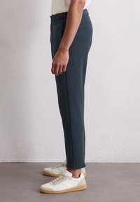Dunkelblaue, maßgeschneiderte Hosen mit schlanker Passform, seitlichen Taschen, einer glatten Textur und einem sauberen Saum, kombiniert mit weißen Sneakers.