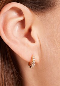 Goldene Creolen mit fünf kleinen, klaren Edelsteinen. Nahaufnahme zeigt Textur, Glanz und ein sicheres Clip-Design.