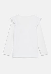 Άσπρο μακρυμάνικο τοπ με βολάν στους ώμους· απαλό βαμβακερό ύφασμα· απλός σχεδιασμός χωρίς σχέδια ή επιπλέον χρώματα.