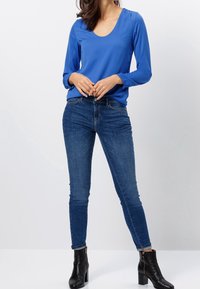 Blaues Langarmoberteil mit einem runden Halsausschnitt, kombiniert mit dunkelblauen Skinny-Jeans und schwarzen Knöchelstiefeln mit einem goldenen Rei�ßverschluss.