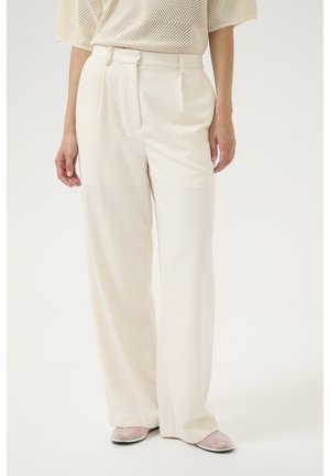 Helle beige Wide-Leg-Hosen aus strukturiertem Stoff. Mit hoher Taille, Falten und Taschen an den Seiten. Kombiniert mit transparenten Schuhen.
