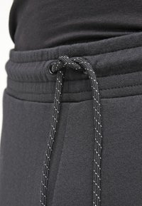 Svart dragsnöre knutet i en rosett på midjan av mörkgrå sweatpants med synlig sömnad och tygstruktur.