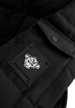 Zwarte gewatteerde jas met een mouw die een gestructureerde patch en een zilveren berenlogo heeft, vergezeld van vier zwarte studs. Gladde stof en gestikte details.