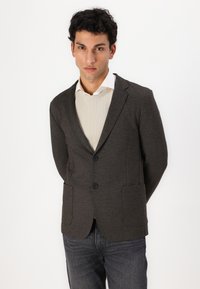 Donkergrijze blazer van zachte stof met een enkelvoudig ontwerp, twee voorkruimels en zwarte knopen, gedragen over een lichtgekleurde shirt.