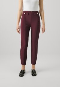 Burgundske krojene hlače s visokim strukom, zlatnim dodatkom, vertikalnim šavovima i uskim krojem, uparene s crnim mokasinama.