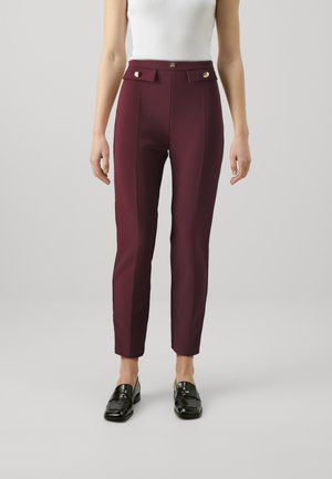 Pantalons ajustés bordeaux à taille haute, avec des accents en métal doré, des coutures verticales et une coupe slim, associés à des mocassins noirs.
