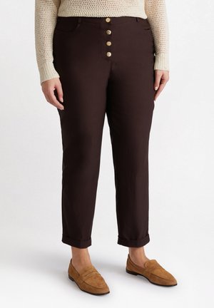 Brown trousers made of cotton with a fitted design, featuring a five-button fly, belt loops, and rolled hems, paired with tan loafers.