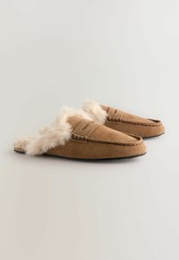 Chaussons en suède brun avec doublure en fausse fourrure, design enfilable et détails couturés sur le dessus. Semelle en caoutchouc noir pour l'adhérence.