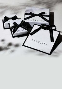 Tres cajas de regalo en blanco con acentos negros. Cada una tiene un lazo de cinta negra, mostrando el nombre de la marca "LATELITA" en letras en negrita.