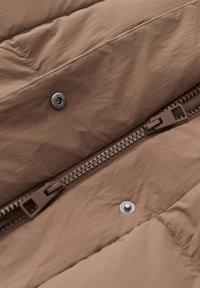 Braun gepolsterter Stoff mit glatter Textur, ausgestattet mit einem Reißverschluss und einer Druckknopfverschluss, sowie horizontalen gesteppten Nähten.