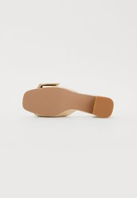 Gullfarget høyhælte sandal med solid plattform og ankelrem. Sålen er lysebrun med en strukturert finish.