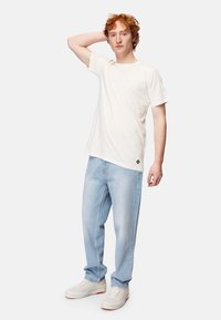 Lys cremefarvet bomulds t-shirt med en afslappet pasform, parret med lyseblå denimjeans. Outfittet er suppleret med hvide sneakers.