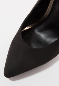 Chaussure femme noire à bout pointu avec une finition mate lisse et une ouverture de bord légèrement incurvée.