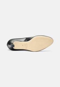 Zapato de tacón alto de cuero negro con punta afilada y textura suave. La suela exterior es beige, con un logotipo y una marca de tamaño.