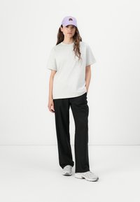 T-shirt gris clair à manches courtes, pantalons larges noirs, et casquette lavande avec broderie florale, portés avec des baskets grises.