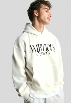 Crèmekleurige hoodie met een voorvak en een oversized pasvorm. Kenmerkt zich door zwarte tekst "AMBITIOUS Souls" over de borst. Zachte textuur.