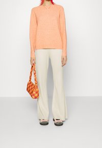 Suéter de punto melocotón, pantalones de campana crema y un bolso a cuadros naranja. Zapatillas con acentos negros. Materiales sencillos y texturizados en toda la composición.