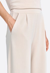 Pantaloni a gamba larga di un beige chiaro, realizzati in tessuto morbido, con tasche laterali e pieghe sottili vicino alla vita.