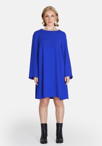 Ein blaues Kleid mit Glockenärmeln aus glattem Stoff, mit einem Rundhalsausschnitt und lockerer Passform, kombiniert mit schwarzen Knöchelstiefeln.