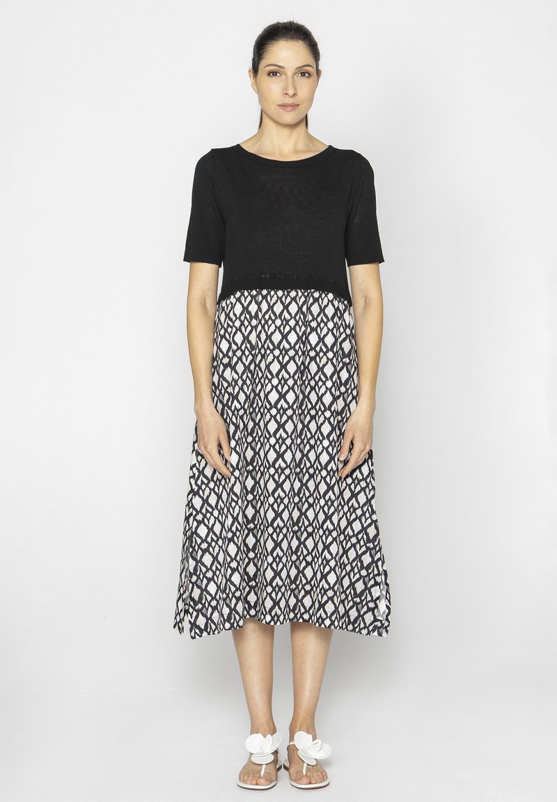 Czarny top z krótkim rękawem z wzorzystą spódnicą w biało-czarnym kolorze, z luźnym krojem i długości do kolan, w połączeniu z białymi sandałami.
