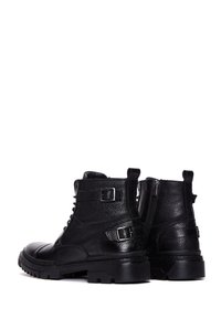Botas de cuero negro con un acabado texturizado, cierre de cordones en la parte delantera, dos hebillas y una suela de goma resistente con un patrón de banda de rodadura robusto.
