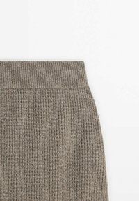 Gros plan sur la partie supérieure d'un vêtement en maille côtelée marron clair avec une large ceinture élastique.