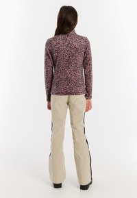 Ružový top s dlhými rukávmi a čiernym leopardím vzorom, skombinovaný s béžovými nohavicami s bočnými čiernymi pruhmi. Hladká textúra, priliehavý strih.