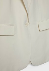 Jasno beżowa marynarka o gładkiej fakturze, z pojedynczym zapięciem na guziki, dwoma przednimi kieszeniami i wyraźnie zarysowanymi klapami.