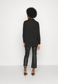 Chemise noire à manches longues avec des rayures verticales, design avec col et détails de bouton, associée à un pantalon évasé en simili cuir noir et des talons à lanières.