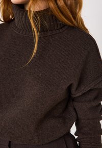 Maglione a maglia marrone scuro con colletto alto a costine e tessuto testurizzato, con maniche lunghe leggermente larghe e una vestibilità comoda.