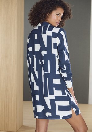 Navy blue shirt dress with white abstract letter print, featuring long sleeves, a collar, and side slits for added mobility. Smooth fabric texture.