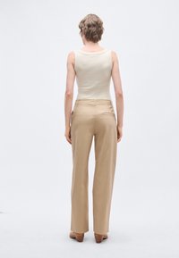 Beežist puuvillasegusest laia lõikega püksid, millel on sile tekstuur, tagataskud ja lõigatud istuvus, kombineeritud varrukateta kreemika ülaosaga.