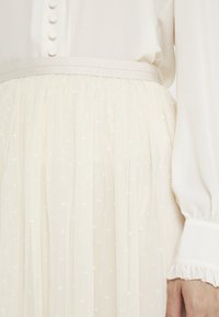 Blouse de couleur claire avec détails de boutons et une jupe taille haute en tulle transparent ornée de délicats motifs d'étoiles blanches et d'une ceinture lisse.