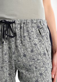 Svetle šedé květinové vzorované kalhoty s šňůrkovým pasem, mají boční kapsy a námořnické akcenty na stranách. Měkká, texturovaná tkanina.