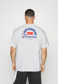 Camiseta de algodón blanca con el texto "Asociación Nacional de Baloncesto" en azul y rojo en la parte de atrás, con un logotipo de Nike en el centro.