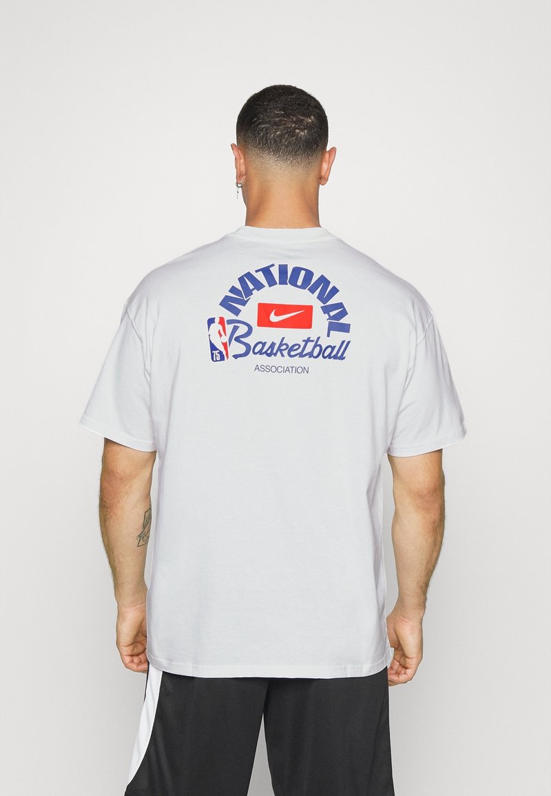 Camiseta de algodón blanca con el texto "Asociación Nacional de Baloncesto" en azul y rojo en la parte de atrás, con un logotipo de Nike en el centro.