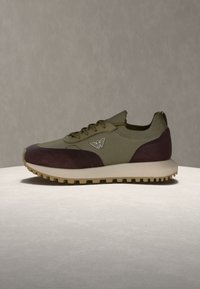 Χαμηλά αθλητικά παπούτσια με δίχτυ σε ελιά πράσινο και πάνελ από σουέντ σκούρο καφέ, μπεζ σόλα και μεταλλικό λογότυπο στο πλάι.