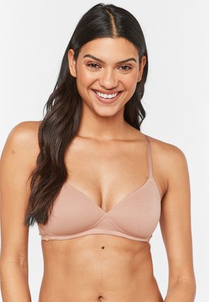 Soutien-gorge seamless rose clair avec des bretelles fines réglables, une texture de tissu lisse et des bonnets triangulaires. Design minimaliste sans matériel visible.