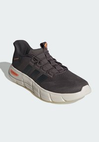 Black athletic shoe with mesh upper, orange accents, and white rubber sole. Features lacing system and textured body for breathability.
