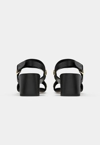 Black leather sandals with a chunky heel, featuring two adjustable straps and gold hardware accents. Smooth texture with a closed back.