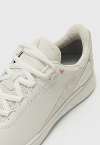 Sneakers brancos à prova d'água com couro texturizado, painéis de malha trançada e atacadores planos. Apresenta um logótipo discreto e uma sola azul clara.
