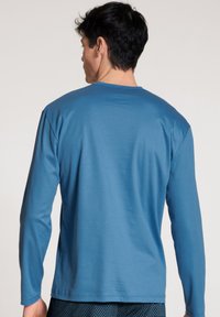 Long-sleeve T-shirt in a solid blue color, made from soft fabric with a relaxed fit. Seamless shoulders and a crew neckline detail.