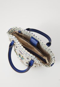 Woven tote bag in blue and white, featuring textured pattern and embellished details. Interior has a zip pocket and spacious main compartment.
