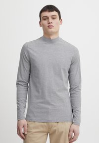 Camisa de manga larga gris claro con cuello alto. Está hecha de una tela suave y elástica. Presenta un corte ajustado y costuras mínimas para un aspecto limpio.